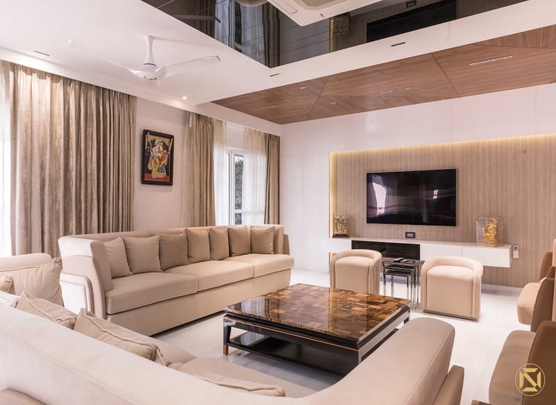 Living room in Hyderabad with beige sofas, glossy stone-top coffee table, wall-mounted TV and coffered ceiling