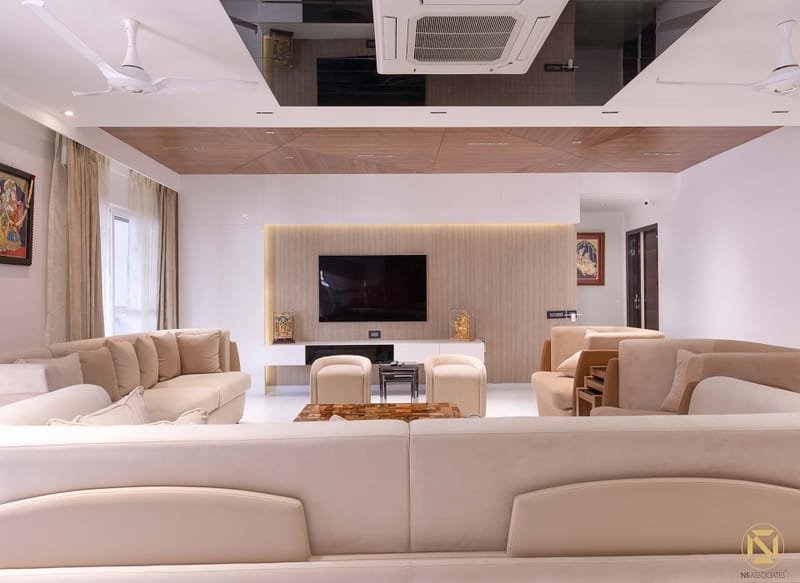 Large living room with cream sectional sofas, wall-mounted TV, fluted wood panel and glossy black ceiling, Hyderabad
