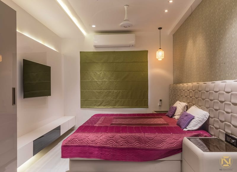 Bedroom with magenta quilt, olive padded wall panel, tufted leather headboard and floating TV unit, Hyderabad