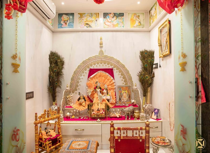 Home pooja room in Hyderabad with ornate silver mandap, deity idols, peacock feathers and pink draped offering table