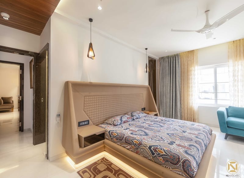 Master bedroom with curved leather bed, paisley bedspread, teal accent chair and wood-slat ceiling, Hyderabad