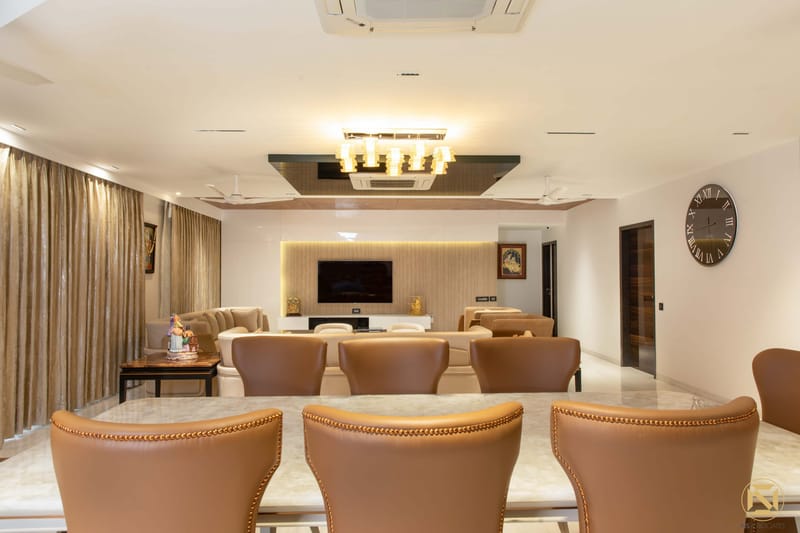Spacious living-dining room with tan leather chairs, backlit TV wall, linear chandelier and wall clock, Hyderabad