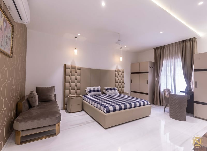 Master bedroom with tufted headboard, checked bedding, grey chaise, fitted wardrobes and draped curtains, Hyderabad