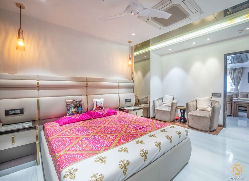Master bedroom in Hyderabad with tall channel-tufted headboard, pink bandhani bedspread and grey lounge chairs