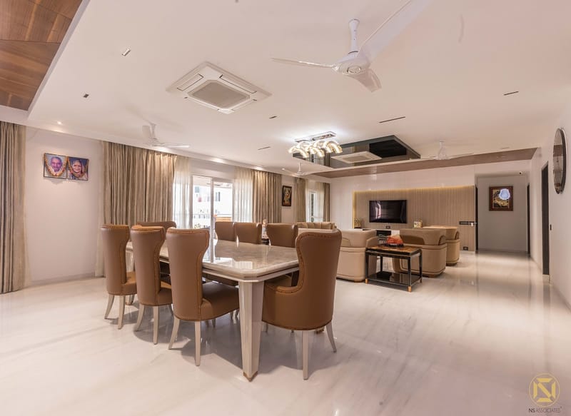 Open dining and living area in Hyderabad with marble dining table, tan leather chairs and beige sofa beyond