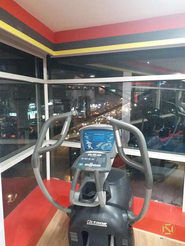 Octane elliptical trainer positioned at a floor-to-ceiling window overlooking a city street at night, Hyderabad
