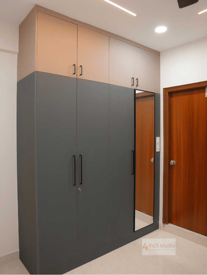 Bedroom wardrobe in charcoal grey and blush laminate with a full-length mirror panel beside a wooden door, Hyderabad