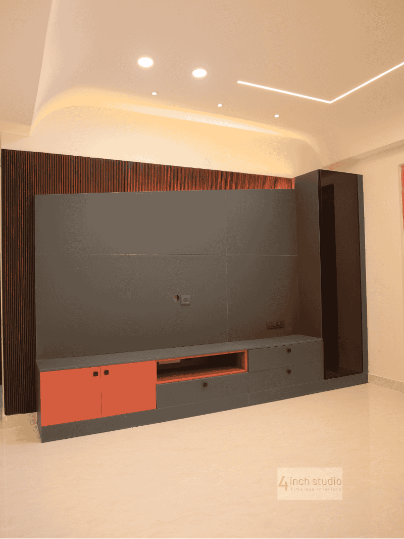 Living room TV unit with grey panel wall, fluted wood backdrop and coral cabinet accents under a curved false ceiling, Hyderabad