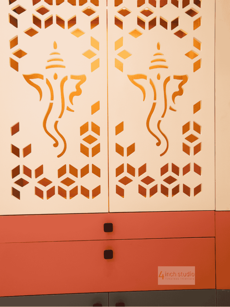 Close-up of white CNC-cut pooja doors with mirrored gold Ganesha and geometric jali above coral drawer fronts, Hyderabad