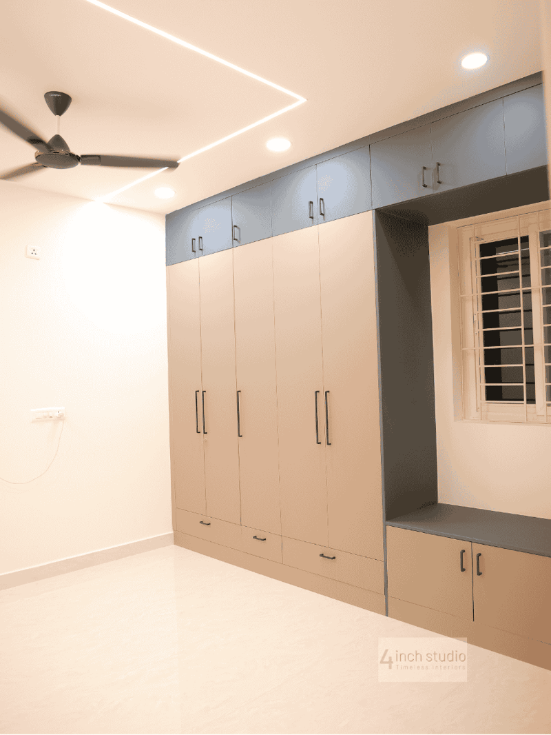 Bedroom wardrobe wall in beige with navy lofts and a cushioned window-seat bench under coffered ceiling, Hyderabad 3BHK