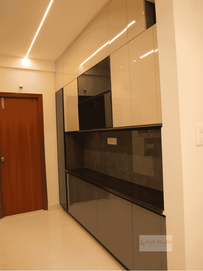 Tall crockery and storage unit in glossy beige and grey laminate with dark stone backsplash beside a flush door, Hyderabad