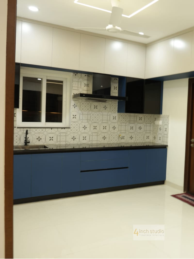 Modular kitchen with navy base cabinets, white uppers, window over the sink and ceiling fan above, Hyderabad