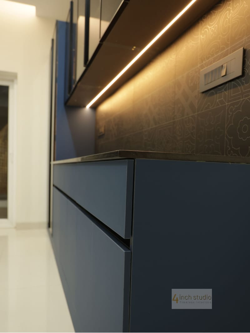 Close-up of a navy-blue cabinet with black granite top, patterned backsplash and warm LED strip in a Hyderabad kitchen