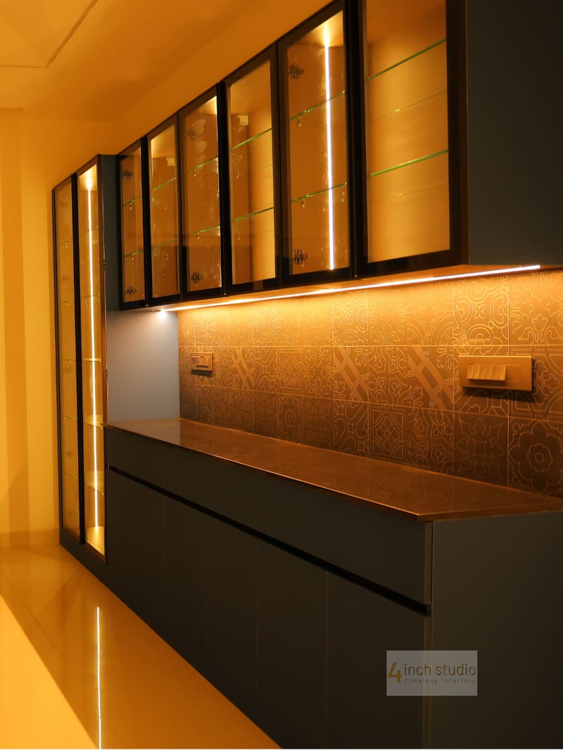 Backlit glass-front crockery unit in charcoal with warm LED glow and patterned tile backsplash, Hyderabad home