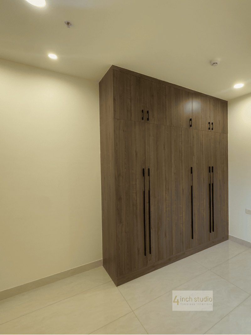 L-corner walnut wardrobe with loft storage and recessed lighting against a pale bedroom wall, Hyderabad
