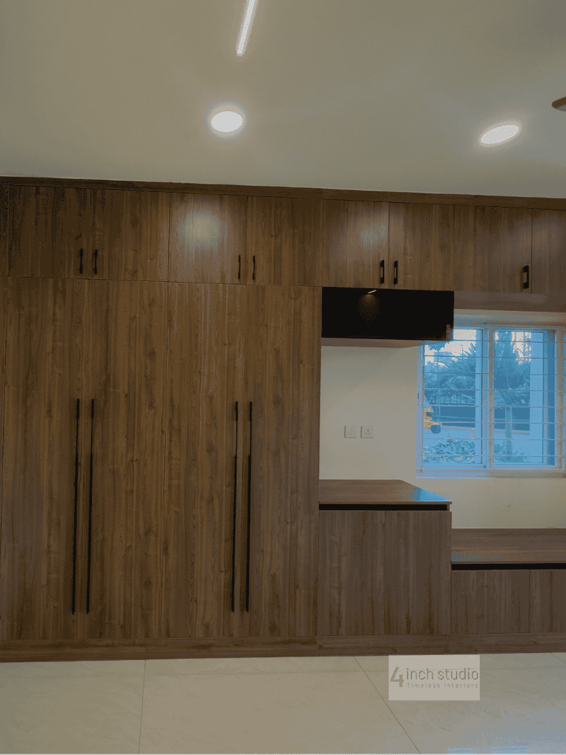 Bedroom wall of dark walnut wardrobes with TV niche and a window-side study ledge, Hyderabad apartment