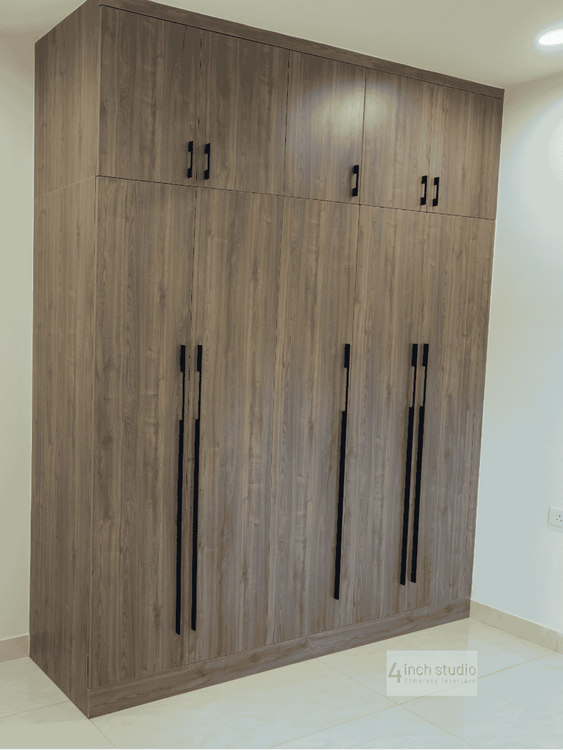 Tall grey-wood wardrobe with overhead loft cabinets and vertical black pulls in a bedroom corner, Hyderabad