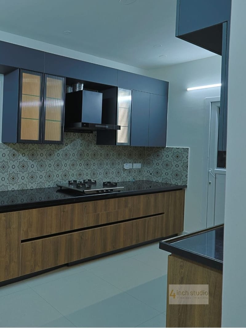 Modern kitchen with navy-blue cabinets, woodgrain base units, patterned Moroccan-tile backsplash and black countertop, Hyderabad
