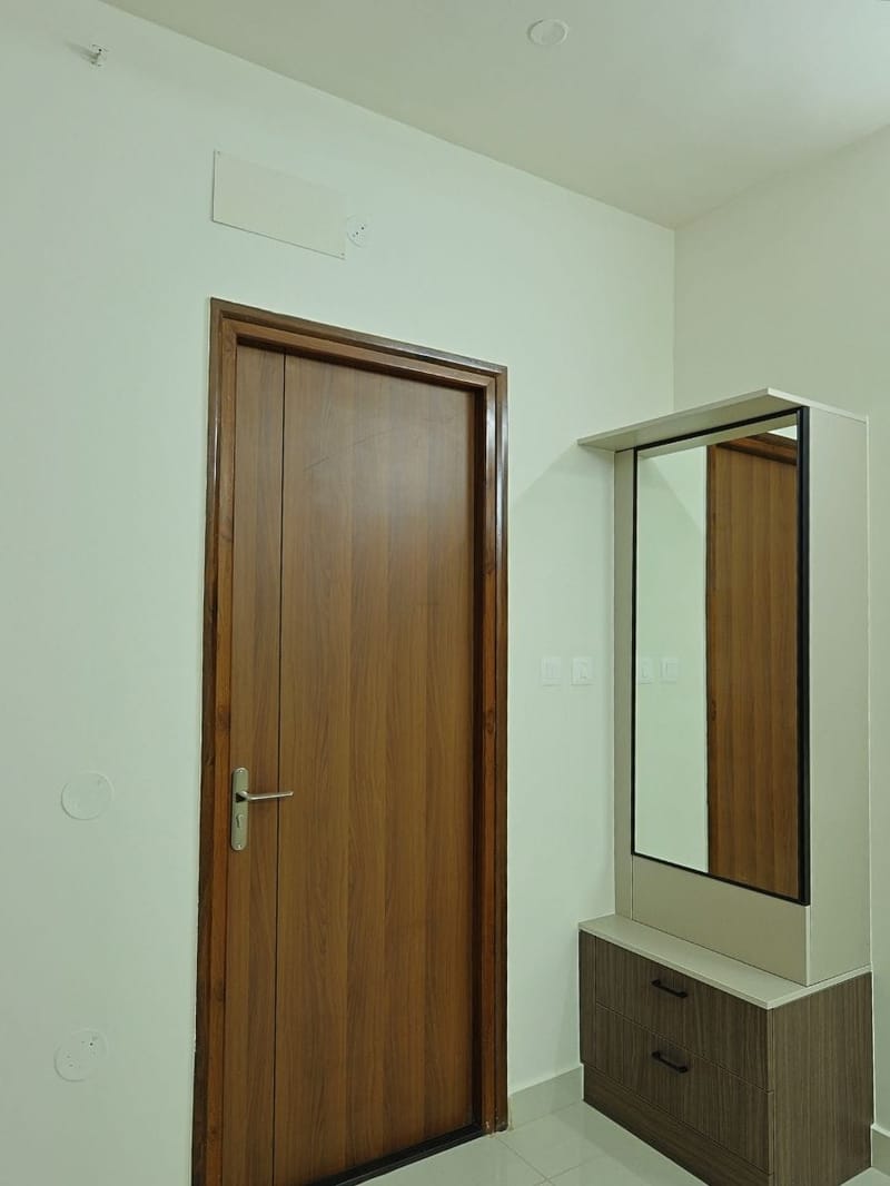 Bedroom corner with teak veneer flush door and wall-mounted mirror over a laminate drawer unit, Hyderabad
