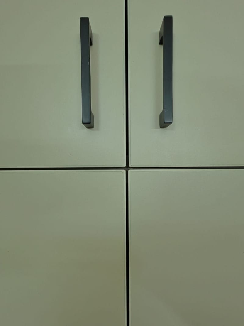 Close-up of off-white cabinet shutters with slim black bar handles and crisp grooved joints, Hyderabad
