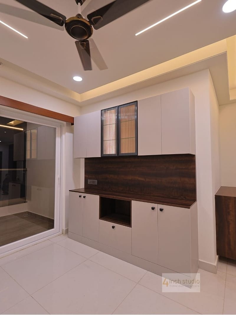 Living-dining storage unit with white cabinets, fluted-glass doors and dark wood backsplash beside a sliding glass door, Hyderabad
