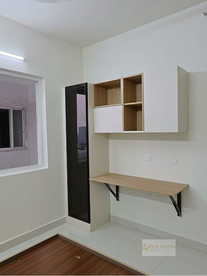 Bedroom study corner with floating wooden desk, open shelf unit and slim tinted-glass tall cabinet by the window, Hyderabad