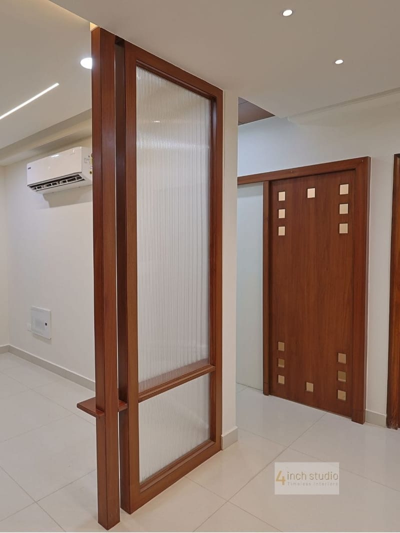 Foyer fluted-glass teak partition beside a panelled teak door with brass square inlays, Hyderabad home