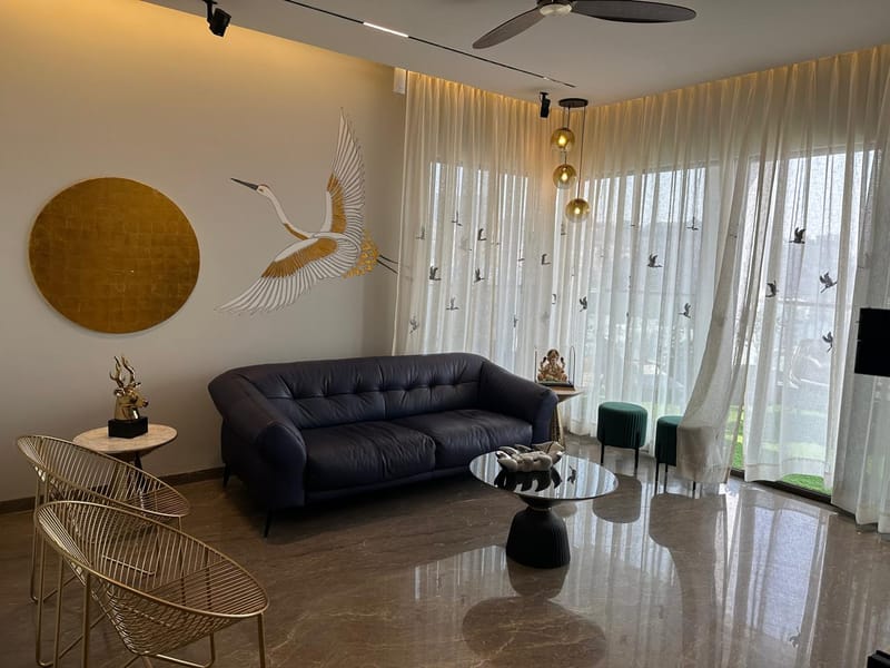 Living room with navy leather sofa, painted crane mural, gold disc wall art and gold wire chairs over marble flooring, Hyderabad