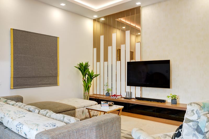 Living room with wall-mounted TV, gold-and-white slatted partition, low wood console and grey sectional, Hyderabad