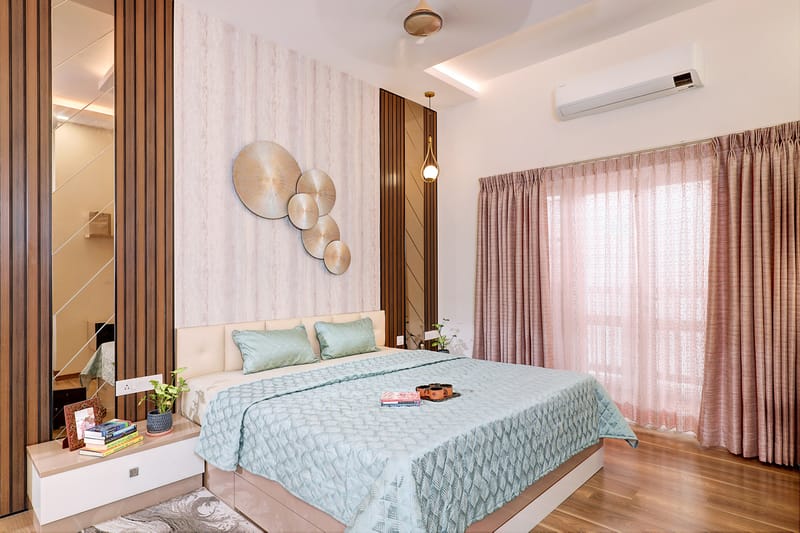 Bedroom with teal bedding, gold disc wall art, sheer pink curtains and wood flooring, Hyderabad