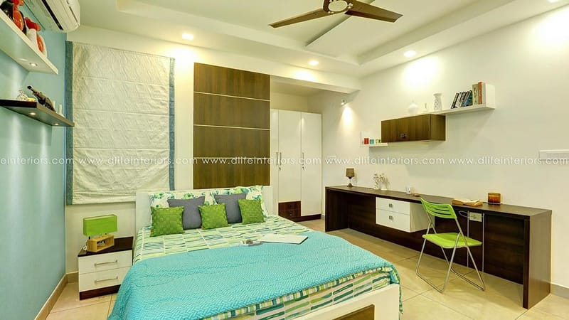 Bedroom with teal accent walls, green-blue bedspread, dark wood study desk and floating wall shelves, Hyderabad
