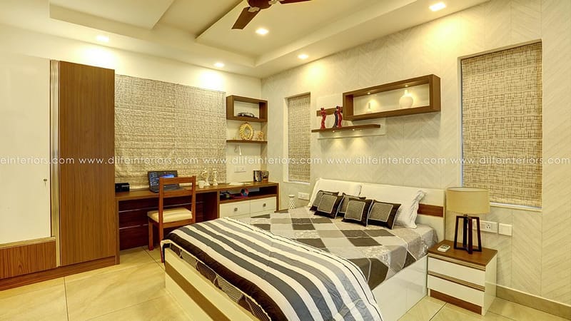Warm-toned bedroom with wood wardrobe, study desk and grey-striped bed, lit wall niches and ceiling fan, Hyderabad