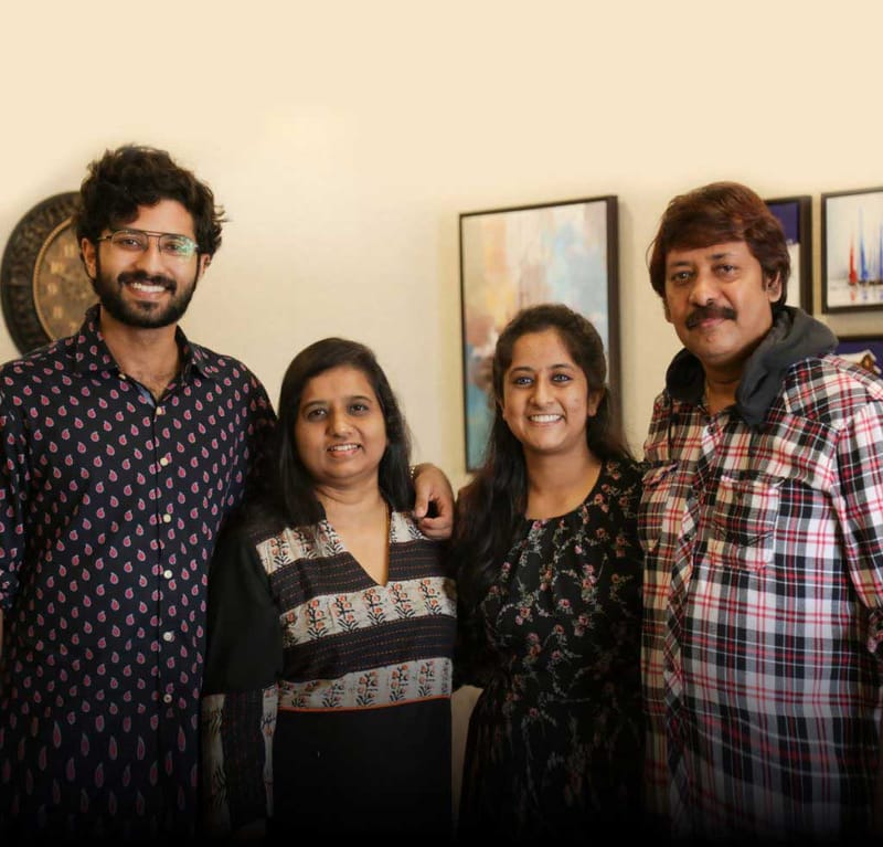 Portrait of a smiling family of four standing together in a living room with framed art behind