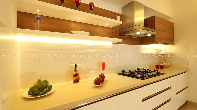 Galley kitchen close-up with glossy white cabinets, walnut floating shelves, gas hob and stainless chimney, Hyderabad