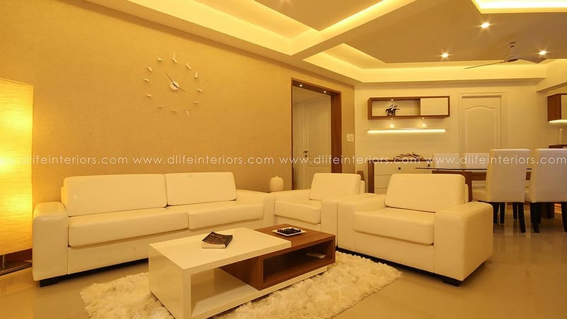 Cream-toned living room with white leather sofa set, low coffee table and a starburst wall clock, Hyderabad
