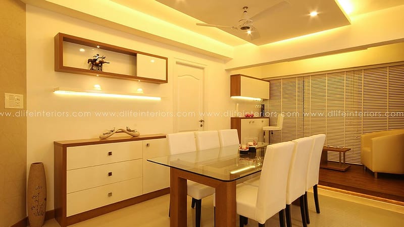 Dining area with glass-top table, white upholstered chairs and a wood-and-white sideboard with display niche, Hyderabad