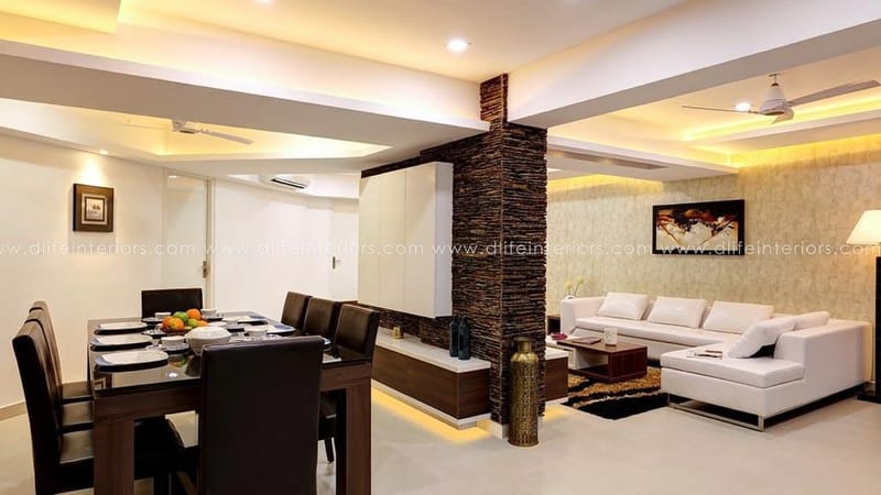Open-plan living and dining in Hyderabad with stone-clad pillar, white L-shaped sofa, dark wood six-seater table and cove lighting