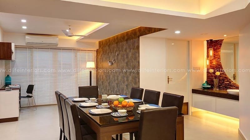 Dining area in Hyderabad with textured stone feature wall, dark wood dining set and warm cove-lit false ceiling