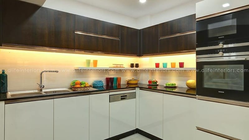 L-shaped modular kitchen in Hyderabad with glossy white units, walnut wall cabinets, black counter and built-in oven