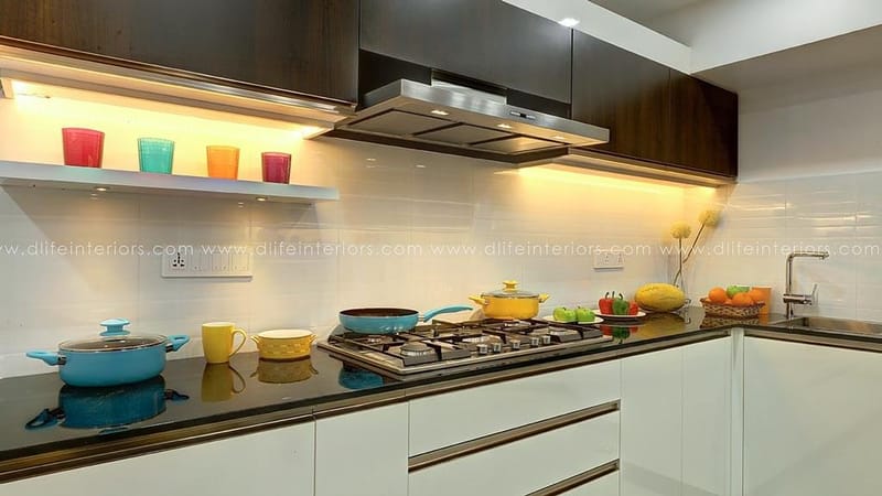 Kitchen counter detail in Hyderabad with five-burner gas hob, stainless chimney, white units and bright cookware on black granite