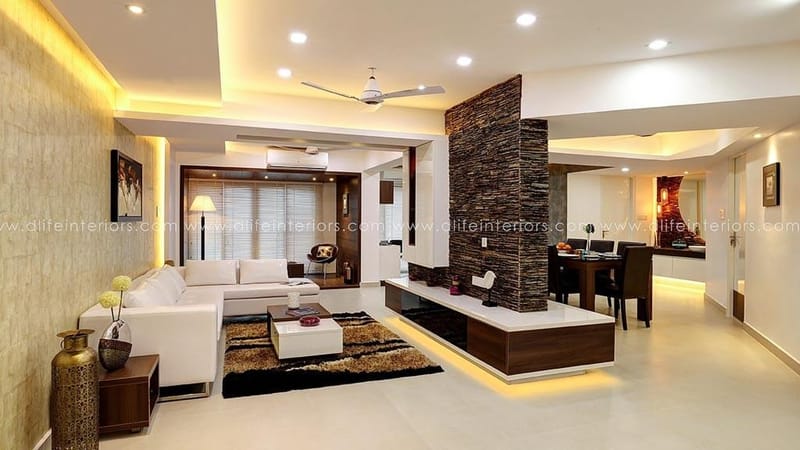 Open-plan living room with sectional sofa, stone-clad partition, layered rug and dining zone under cove lighting, Hyderabad