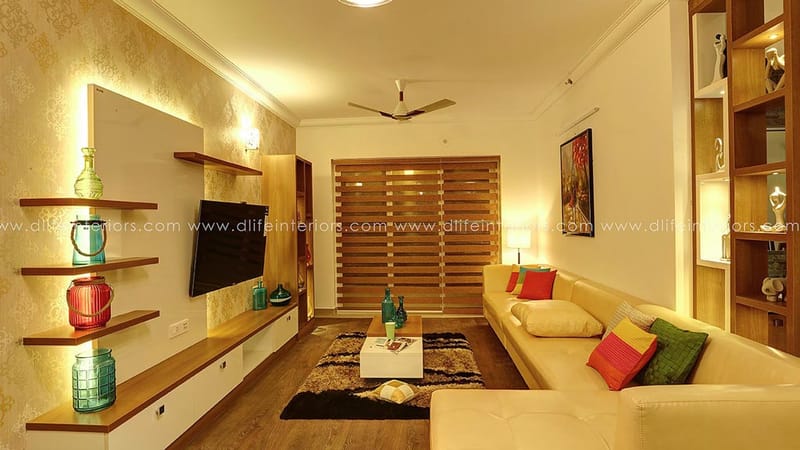 Living room with wall-mounted TV on floating wood shelves, beige sofa, patterned rug and gold textured wall, Hyderabad