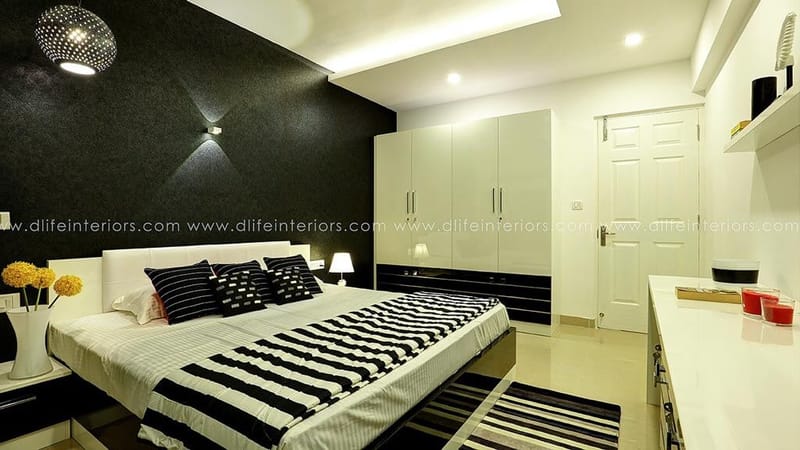 Master bedroom with dark textured accent wall, glossy white wardrobes and black-and-white striped bedding, Hyderabad