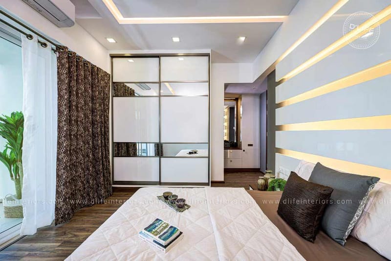 Bedroom with mirrored sliding wardrobe, backlit grey-and-white striped feature wall and warm wood flooring, Hyderabad