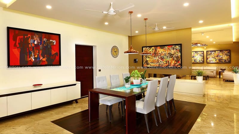 Dining room with long wood table, white upholstered chairs, marble floor and vivid framed paintings, Hyderabad
