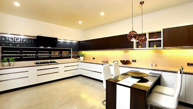 L-shaped modular kitchen in white and dark wood with copper pendant lights and a breakfast bar, Hyderabad