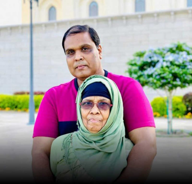 Portrait of two people standing outdoors before a pale building with a manicured garden behind them