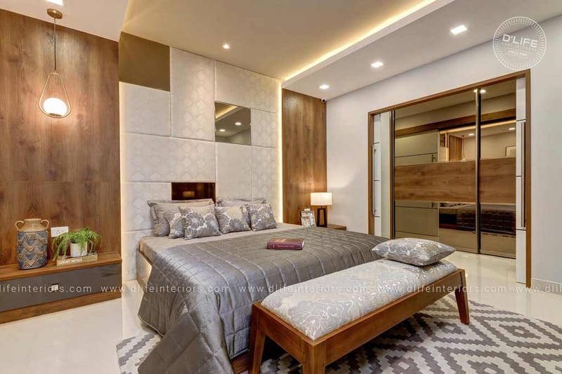 Master bedroom in Hyderabad with quilted grey bedding, geometric headboard panels, mirrored wardrobe and wood bench