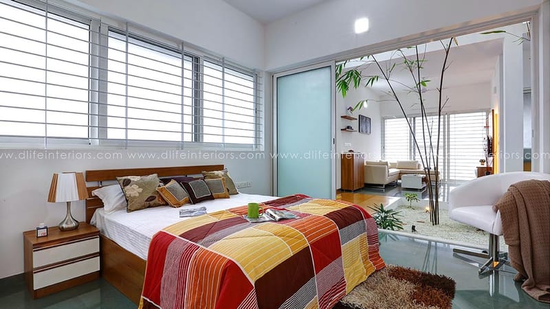 Bedroom with striped orange bedspread, frosted glass partition, bamboo plant and white lounge chair, Hyderabad