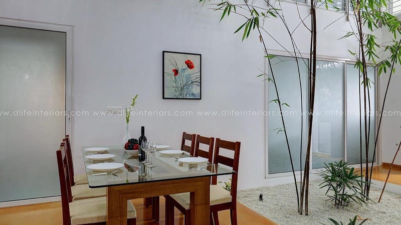 Dining nook with glass table, wooden chairs, floral artwork and frosted-glass doors framing bamboo, Hyderabad
